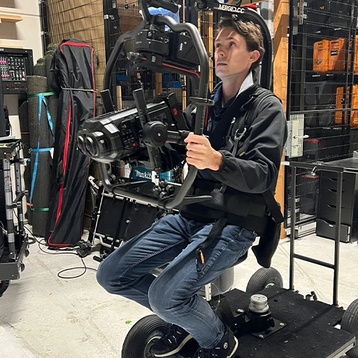 Rick Cosijn seated on a camera dolly, wearing an EasyRig support system, operating a DJI Ronin 2 gimbal with a Blackmagic URSA Cine Immersive camera mounted.