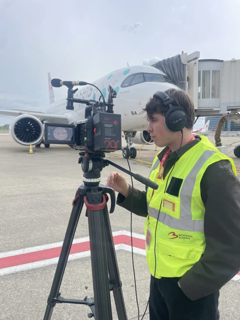Marijn Mannien from Cinaglyph wearing headphones while operating the Blackmagic URSA Cine Immersive camera on the tarmac next to a Brussels Airlines Airbus A320neo.